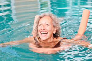 An older woman swims with a pool noodle for support during stroke recovery