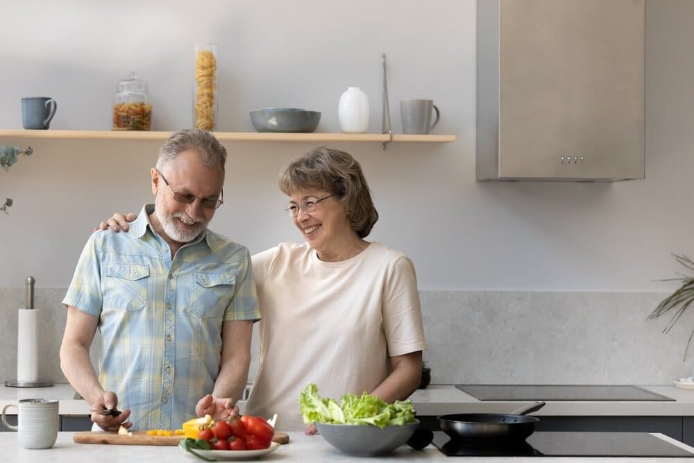 A husband and wife smile and laugh while cooking in their fall proofed kitchen